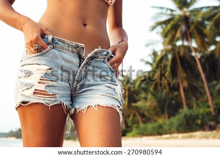 Fashion woman in jeans shorts posing on the beach. Outdoors lifestyle