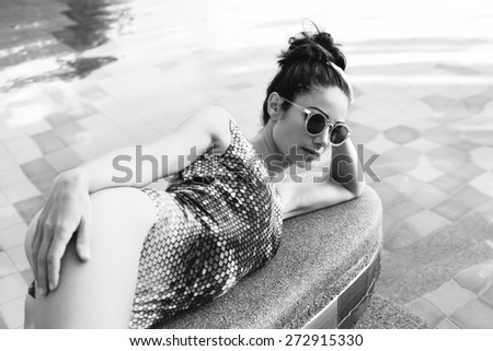 Young pretty woman with perfect tanned body lying on yellow air mattress in the pool in summer and having fun. Outdoor fashion portrait of happy girl
