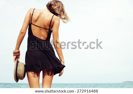 Outdoor summer sunny fashion portrait of pretty young sensual woman posing in black dress on the rocks on the ocean seashore. Outdoors lifestyle portrait