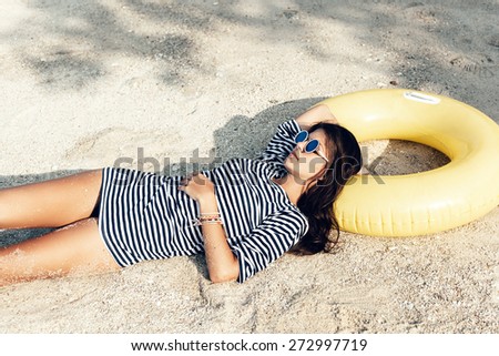 Beautiful woman in sunglasses lying on a beach in sand at summer day. Outdoor lifestyle portrait of girl