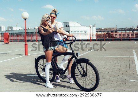 two young women taking selfie with mobile phone. Swag teen girls on black bike. Outdoor lifestyle portrait