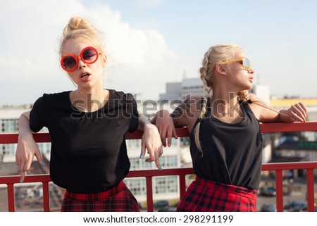 portrait of two pretty hipster blonde sisters  wearing plaid skirt and  black T-shirt. Girls smile, have fun against  urban city.