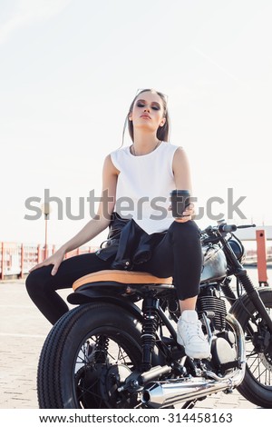 Young sexy girl sitting on vintage custom motorcycle and drinking coffee . Outdoor lifestyle portrait