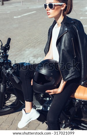 Biker girl sitting on vintage custom motorcycle. Outdoor lifestyle portrait