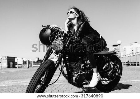 Biker girl sitting on vintage custom motorcycle. Black white Outdoor lifestyle portrait