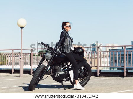 Biker girl in leather jacket sitting on vintage custom motorcycle. Outdoor lifestyle portrait