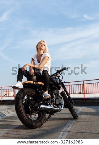 Biker sexy woman sitting on vintage custom motorcycle. Outdoor lifestyle portrait