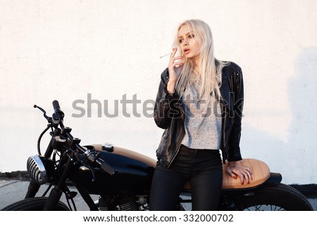 Fashion female biker girl. Young blonde woman sitting on vintage motorcycle and smoking cigarette. Outdoors lifestyle portrait
