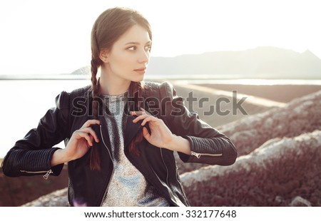 Young sexy woman with braids dressed in a silver dress and leather jacket. Fashion girl enjoying stunning views of the slope. Outdoors lifestyle portrait