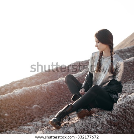 Fashion girl enjoying stunning views of the slope. Young sexy woman with braids dressed in a silver dress and leather jacket. Outdoors lifestyle portrait