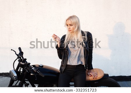 Female biker girl smoking cigarette. Young woman sitting on vintage motorcycle. Outdoors lifestyle portrait