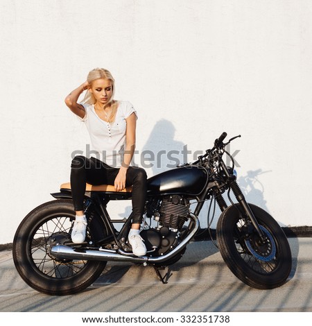 Fashion female biker girl. Young Blonde woman in leather jacket sitting on vintage custom motorbike. Outdoors lifestyle portrait
