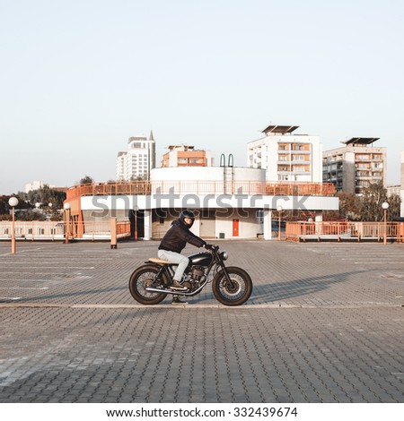 Biker riding on a motorcycle in the parking lot in the city with open sky on background. Vintage custom motorbike