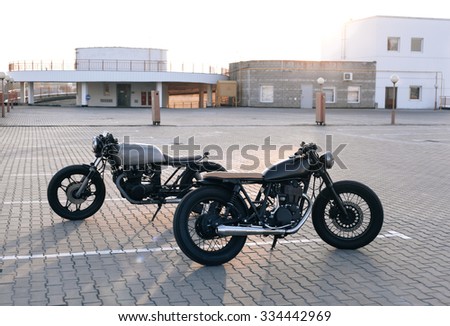 Two vintage custom motorcycles in the parking lot during sunset. Road and city with open sky on background.