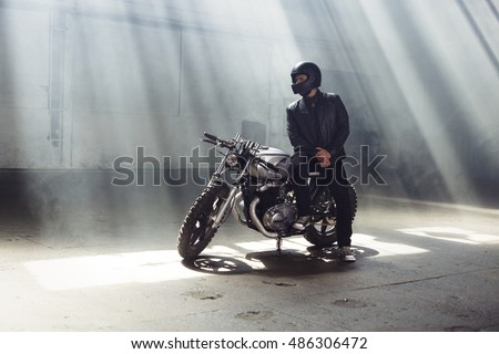 Sexy biker man wearing jeans and leather jacket sitting on vintage custom motorcycle. Urban scene