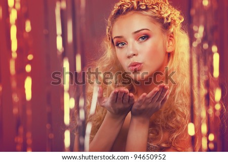 Beautiful young girl with blond curly hair standing behind a curtain made of golden ribbons