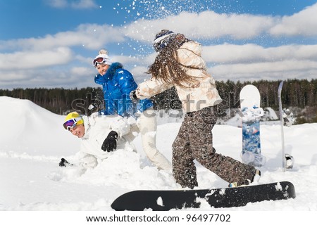 Three young people are having fun on the snow, throwing snow at each other