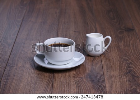 Mug with black coffee and milk jug on the wooden background