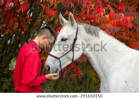 Portrait of a nice white horse and young man on autumn background