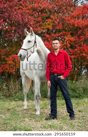 Portrait of a nice white horse and young man on autumn background