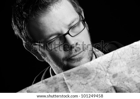 Lost - This is a high contrast black and white image of a young man concerned and looking down at a map. Shot with hard light on a black background.