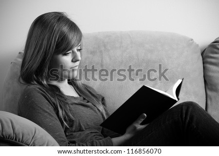 Reading - This is a black and white photo of a young woman sitting on a couch enjoying a good book.