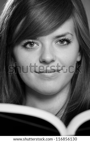 Student - This is a close up black and white photo of a cute young woman holding a book. Shot with a shallow depth of field.