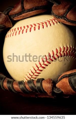 Baseball - This is a close up shot of an old baseball inside an old baseball glove on a wood background. Shot in a warm retro color tone.