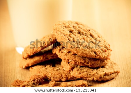 Cookies - This is a photo of a pile of homemade oatmeal cookies with crumbs shot on a wooden cutting board in front of a glass of milk. Shot with a shallow depth of field in a warm retro color tone.