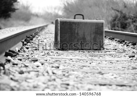 Suitcase On Railroad Tracks - This is a high contrast black and white photo of an old retro suitcase sitting on a set of railroad tracks.