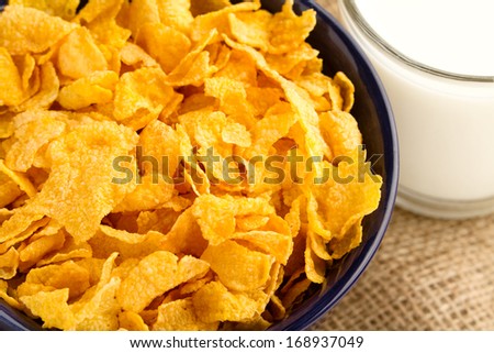 Corn Flaked Breakfast Cereal - This is a high angle shot of a bowl of cereal and a glass of milk. Shot with a burlap background and a shallow depth of field.