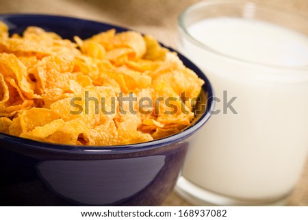 Corn Flaked Breakfast Cereal - This is a shot of a bowl of corn flake cereal and a glass of milk shot with a shallow depth of field with a burlap background.
