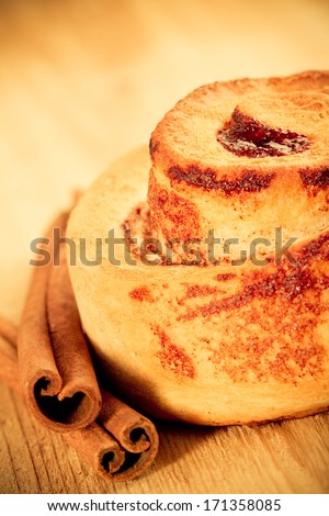 Cinnamon Roll - This is a shot of a tasty cinnamon roll sitting on a wooden table next to a couple cinnamon sticks. Shot in a warm retro color tone with a shallow depth of field.