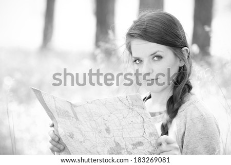 Young Woman Reading Map - This is a high contrast black and white photo of a cute young woman sitting in tall grass in the woods reading a map.