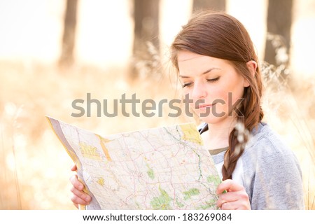 Young Woman Reading Map - This is a photo of a cute young woman sitting in tall grass in the woods reading a map.