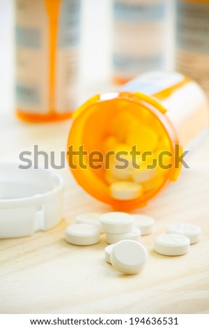 Prescription Pills - This is a high key shot of prescription pills spilling out from their bottle onto a wooden table top. Shot with a shallow depth of field. (Focus Set On Pills)