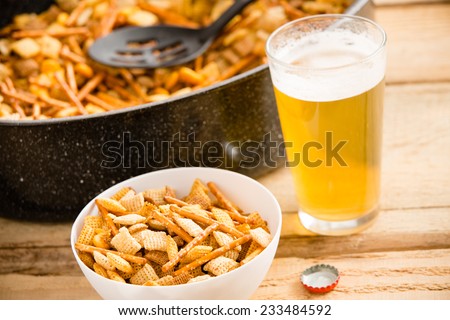 Snacks and Beer - This is a shot of a cold beer sitting next to a party mix. Shot on a wooden table.