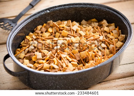 Holiday Party Food Mix - This is a shot of a party mix containing cereal, peanuts and pretzels in a roaster pan on an old wooden table.