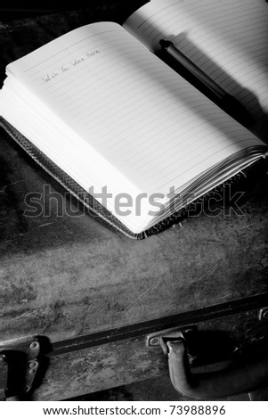 This is a high contrast, black and white shot of an old suitcase with a journal sitting on top.
