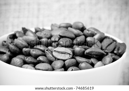 This is a high contrast, black and white shot of roasted coffee beans inside a coffee cup with a burlap sack background. Shot with a shallow depth of field.