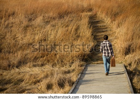 This is a photo of a young man walking down a path with a suitcase.