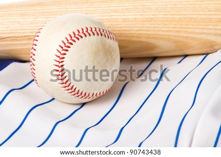This is a shot of an old baseball sitting on a baseball jersey next to a wooden baseball bat.