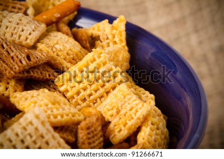 Party Mix... This is a close up shot of a party mix containing cereal and pretzels in a blue bowl with a burlap sack as a background. Shot with a shallow depth of field.