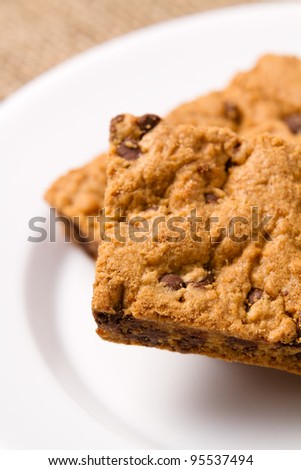 Chocolate Chip Cookie Bar - This is a close up shot of homemade chocolate chip cookie bars on a white plate with a burlap sack background.