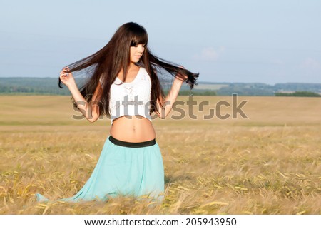 young beautiful long haired girl in a skirt and blouse posing on a background field with ears. Photo toned light yellow to give summer atmosphere