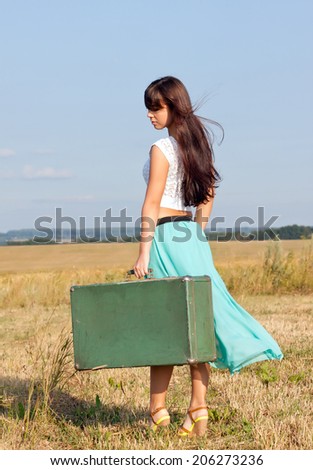 Young girl goes in summer attire comes with a suitcase in hand, goes  on the  field