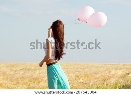 young beautiful long haired girl with balloons in hand posing on a background field with ears.