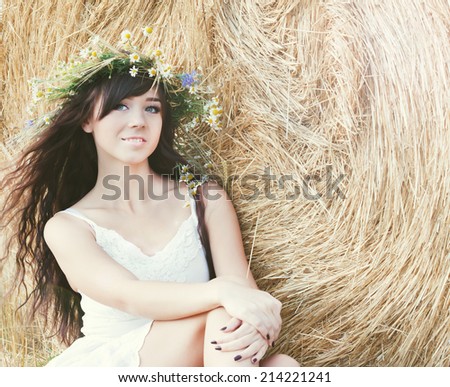 beautiful young country girl in a short dress posing on a summer day sitting on a background of haystack.Photo tinted light yellow to transfer summer atmosphere
