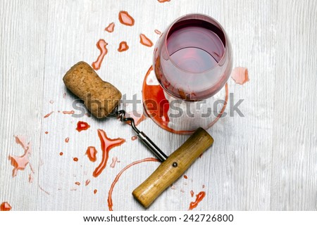 glass of wine and a corkscrew with cork wood surface with stains from wine