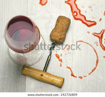 glass of wine and a corkscrew with cork from wine stains on the table.toned